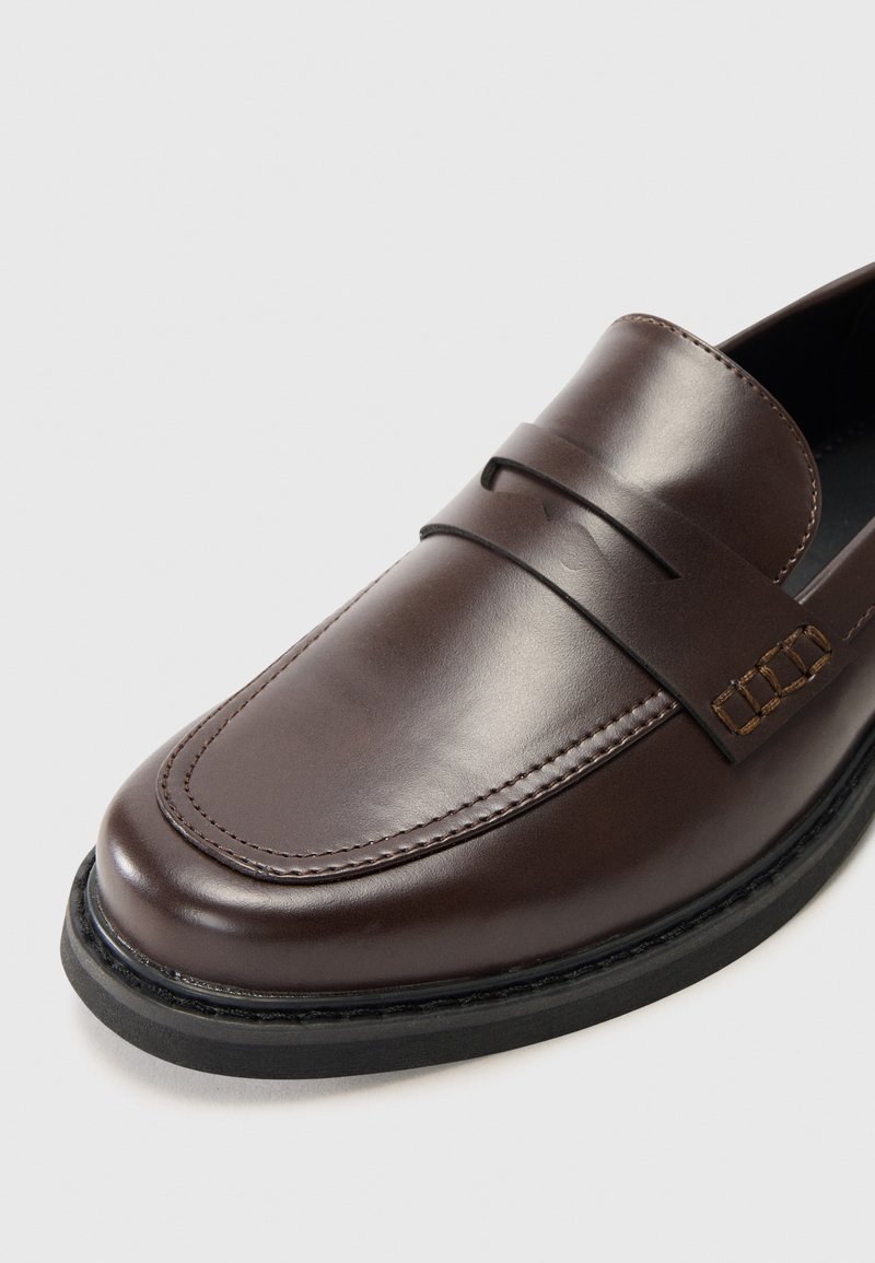 Mocassini in pelle marrone con finitura liscia, dotati di una fascia frontale e cuciture dettagliate, montati su una suola in gomma nera.