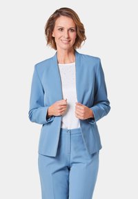 Lichtblauwe jacket met een slanke pasvorm, gesloten halslijn en lange mouwen; gecombineerd met een witte top met subtiele versieringen en bijpassende broek.