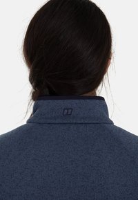 Navyblauwe fleece pullover met hoge kraag, voorzien van een gestructureerd oppervlak en een klein logo nabij de kraag.