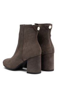 Par de botines de ante marrón oscuro con tacones de bloque y detalles de botones plateados en la parte superior trasera.