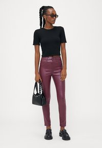 Top preto de malha canelada com mangas curtas, calças bordô brilhantes, mala preta com tachas e sapatos pretos robustos. Silhueta simples e ajustada.