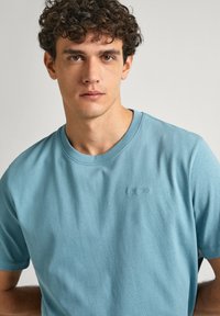 Jasnoniebieska bawełniana koszulka z krótkim rękawem, okrągłym dekoltem i haftowanym logo na piersi, charakteryzująca się gładką teksturą.