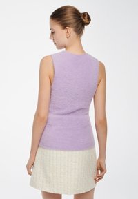 Lila mouwloos topje in een zachte, pluizige textuur, gecombineerd met een crèmekleurige tweed mini-rok met een ruitenpatroon. Schoon lijnontwerp.