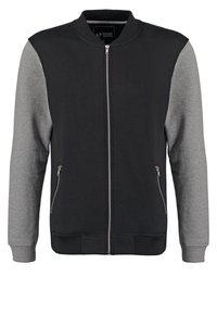 Černá bomber bunda s šedými rukávy; disponuje předním zipem, žebrovaným lemem a dvěma bočními kapsami. Vyrobena z měkké látky s hladkým povrchem.