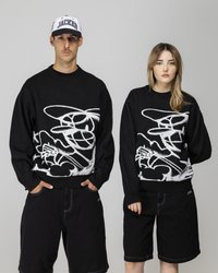 Svarte strikkede genser med et hvitt abstrakt design, kombinert med svarte shorts. Den mannlige modellen har på seg en svart og hvit caps.