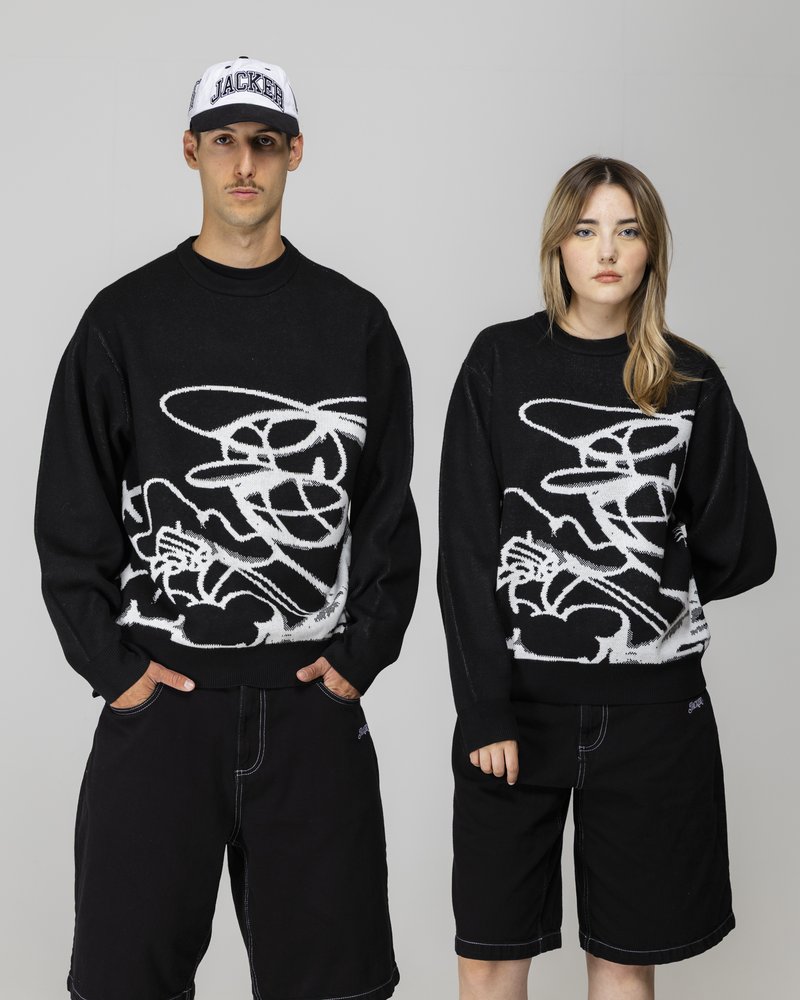Svarte strikkede genser med et hvitt abstrakt design, kombinert med svarte shorts. Den mannlige modellen har på seg en svart og hvit caps.