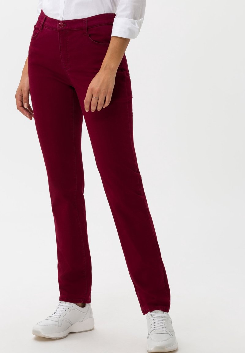 Pantalons en coton bourgogne avec une coupe droite, dotés de poches avant, d'une fermeture à bouton, portés avec des baskets blanches.