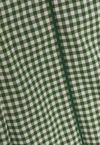 Grün-weißes Gingham-Gewebe mit einem karrierten Muster, einer glatten Textur und einer vertikalen grünen Naht, die in der Mitte verläuft.