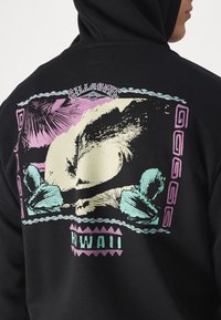 Black hoodie featuring a graphic print of a wave and palm trees in pastel pink, green, and cream colors, with "HAWAII" text at the bottom.