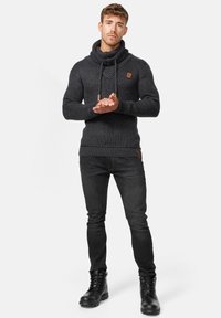 Ciemnoszary sweter ze ściągaczami, z dekoltem w stylu cowl, sznurkami i skórzaną naszywką, w zestawie z czarnymi dżinsami i butami ze sznurowaniem.