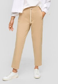 Beige cropped broeken met een trekkoord in de taille, frontzakken en een ontspannen pasvorm, gecombineerd met witte sneakers. Glad stoffen textuur.
