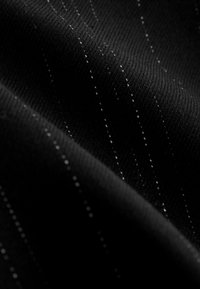 Gros plan sur un tissu noir avec de fines rayures blanches espacées de manière homogène, courant en diagonale sur une surface texturée.