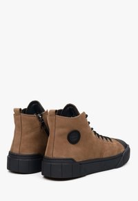 Bruine suède high-top sneakers met zwarte rubberen zolen, voorzien van zwarte veters, een ritssluiting en een rond logo op de hiel.