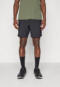 Calções atléticos pretos feitos de tecido leve, com bolsos laterais, combinados com uma camisa verde, meias pretas e sapatos pretos.