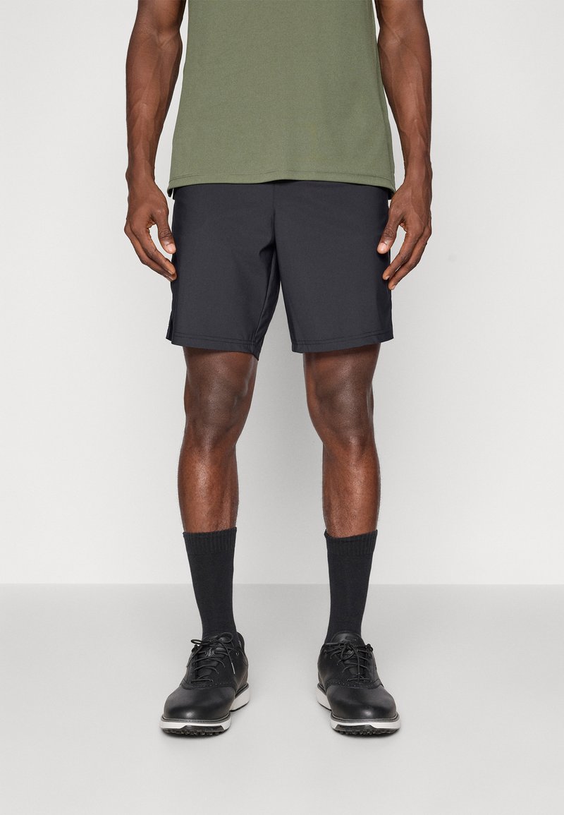 Calções atléticos pretos feitos de tecido leve, com bolsos laterais, combinados com uma camisa verde, meias pretas e sapatos pretos.