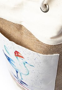 Leinen-Tote-Bag mit beigem Juteboden und einer weißen Stofftasche, die eine bunte Vogelillustration zeigt. Sichtbares Metallösen-Detail.