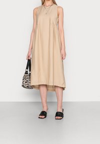 Beige bezramínková šaty s asymetrickým lemem, vyrobené z měkké tkaniny. V kombinaci s tkanými černými sandály na klínku a taškou s černo-bílým zebřím potiskem.