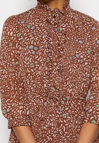 Braun gemustertes Hemd mit Rüschenkragen und Knopfleiste. Verfügt über ein florales Design in Blau und Grün, mit einer taillierten Detail.
