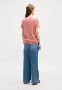 Lys rosa bomulls t-skjorte med korte ermer, kombinert med vide blå denimbukser. Begge plaggene har en avslappet passform.