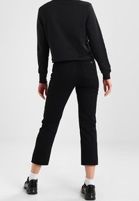 Sweatshirt noir court avec un col rond associé à un jean noir taille haute, slim-fit, avec une coupe droite et des détails de couture subtils.