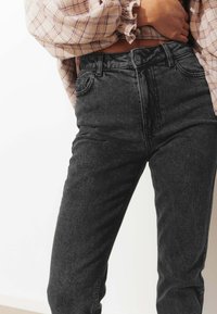 Jean en denim gris foncé taille haute avec une texture lisse, dotée de poches avant et d'une fermeture à bouton à la taille.