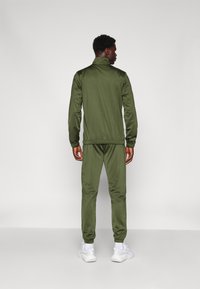 Olijfgroen trainingspak van gladde stof, met een ritsjack met een staande kraag en bijpassende tapered broek met elastische boorden.