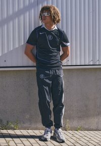 Black athletic jersey with purple accents, gray athletic pants, and gray sneakers, displayed against a textured wall.