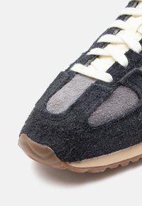 Svart og grå sportsko med en teksturert overdel og glatte detaljer, med hvite lisser og en beige gummisåle.