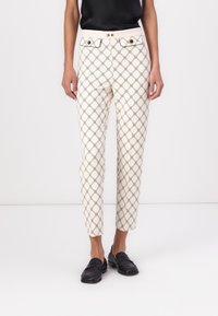 Bele hlače z belim vzorcem in črnim geometrijskim dizajnom, vsebujejo prilegajoč kroj, zanke za pas in zlate dodatke na pasu.