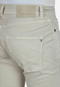 Beige chinos met een gladde textuur, zij- en achterzakken, platte naden en een leren patch met "pierre cardin" branding.