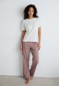 T-shirt à manches courtes crème associé à un pantalon large rose. Design simple, texture douce, coupe décontractée et sans motifs ni embellissements visibles.
