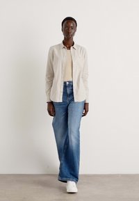 Light grey button-up shirt, beige top, blue wide-leg jeans, white sneakers. Smooth fabric, structured design, casual fit.