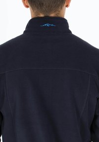 Marineblaue Fleecejacke mit hohem Kragen und blauem Berglogo auf der Rückseite. Sie verfügt über flache Nähte und einen weichen, strukturierten Stoff.