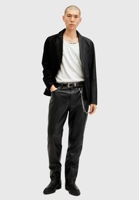 Zwarte leren blazer en broek, met een zilveren kettingdetail op de riem. Witte t-shirt eronder, met een ronde hals.