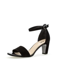 Sandales à talons en daim noir avec un bout ouvert, une bride de cheville et une boucle circulaire en argent. Le talon est de style bloc avec une finition mate.