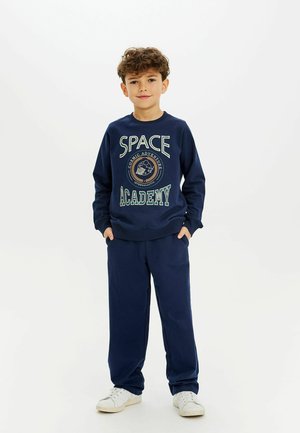 Námornícky modrý sweatshirt s potlačou "SPACE ACADEMY", zmes bavlny, voľný strih; skombinovaný s zodpovedajúcimi námorníckymi teplákmi a bielymi teniskami.