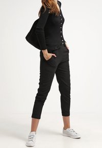 Czarna prążkowana bluzka z długim rękawem na guziki, zestawiona z czarnymi zwężanymi spodniami i białymi tenisówkami. Gładka faktura, dopasowany krój.