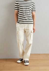 Camiseta de manga corta a rayas en gris y blanco; pantalones cargo en beige con bolsillos laterales; zapatillas negras y blancas con un patrón.