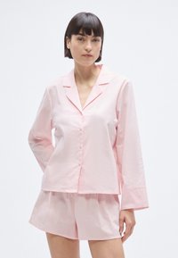 Ensemble de pyjama en coton rose comprenant une chemise à manches longues avec col cranté et boutons, assortie à un short. Texture lisse, coupe décontractée.