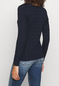 Mörkblå kabelstickad tröja med långa ärmar, ribbade muddar och fåll, med ett strukturerat mönster och en figurnära silhuett.