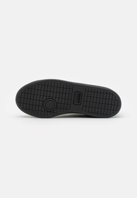 Semelle de chaussure en caoutchouc noir avec un motif de grip texturé, comportant un détail de logo rond et un bord lisse.