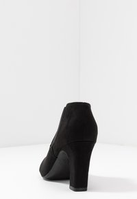 Černá semišová dámská vysoká bota s křivým podpatkem, kulatou špičkou a elastickým materiálem na vnitřní straně pro pohodlné nošení.