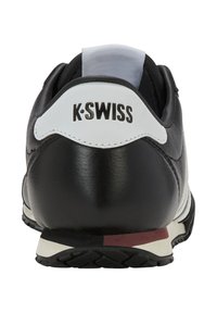 Černé kožené tenisky s bílým poutkem na patě s logem "K-Swiss". Zaoblený tvar, texturovaný povrch, gumová podrážka s kontrastními akcenty.