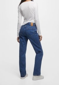 Jeans de mezclilla azul de pierna recta con bolsillos traseros, que presentan un parche de cuero marrón en la cintura y una textura ligeramente desgastada.
