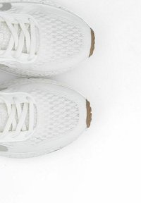 Scarpe da ginnastica bianche con una tomaia in mesh testurizzato, lacci piatti e una suola in gomma marrone chiaro, caratterizzate da un accento di logo minimale.
