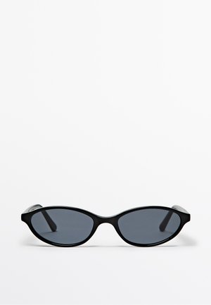 Schwarze ovale Sonnenbrille mit dünnem Rahmen und dunklen Gläsern auf weißem, einfachem Hintergrund dargestellt.