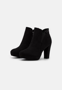 Botas de tobillo de ante negro con tacones cuadrados, cremallera lateral y paneles elásticos sobre un fondo blanco.