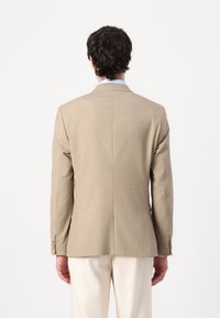 Beige blazer met een gladde textuur, gestructureerde schouders, een enkele rugventilatie en knopen aan de mouwen. Geplaatst tegen een effen witte achtergrond.