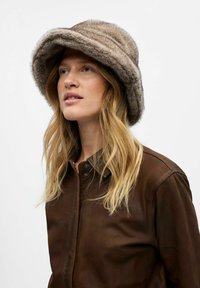 Brauner Kunstfell-Bucket-Hat mit einer weichen, strukturierten Oberfl�äche und einem breiten Rand, kombiniert mit einer braunen Lederjacke.