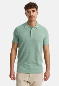 Minzgrünes Polohemd mit kurzen Ärmeln, strukturiertem Strick, zwei-Knopf-Leiste und gerippten Kragen- und Saumdetails. Kombiniert mit hellen Hosen.